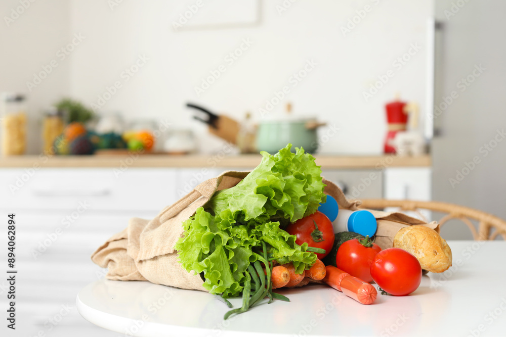 Vegetables, milk and bread in eco bag on table in kitchen
