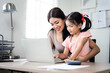 © NAMPIX - Young smiling asian  mother working from home using laptop computer while taking care of her little daughter