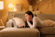© Pixel-Shot - Young woman in pajamas lying on soft couch and chatting with modern laptop in living room at night