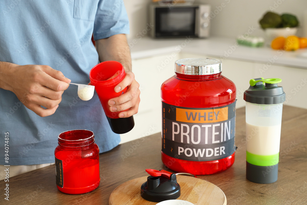 Sporty young man with protein powder in kitchen, closeup