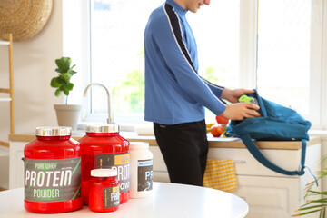 Canvas Print - Jars with protein powder on table of sporty man in kitchen, closeup