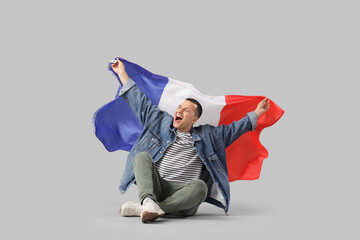 Canvas Print - Happy young man with flag of France sitting on grey background