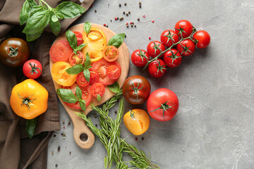 Poster - Wooden board with slices of different fresh tomatoes, basil, rosemary and peppercorn on grey background