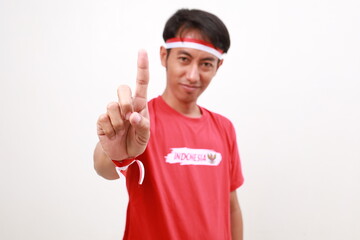 Asian young boy with red white ribbon for celebrating Indonesia independence day standing while showing a finger. Selective focus on hand