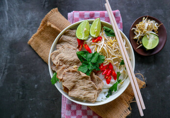 A Bowl Pho Bo traditional Soup with beef, rice noodles, ginger, lime, chili pepper in bowl. Close up. Vietnamese cuisine served on black background