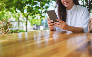 Wall Mural - Closeup image of a young woman holding and using mobile phone in the outdoors