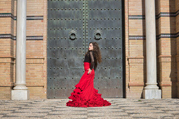 Canvas Print - Young, beautiful, brunette woman in black shirt and red skirt, dancing flamenco in front of an old, black metal door. Flamenco concept, dance, art, typical Spanish.