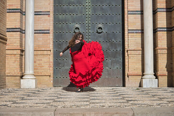 Canvas Print - Young, beautiful, brunette woman in black shirt and red skirt, dancing flamenco in front of an old, black metal door. Flamenco concept, dance, art, typical Spanish.