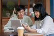 © bongkarn - A young Asian woman is using a calculator while discussing work with her male colleague at a cafe.
