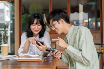 Wall Mural - Two happy young Asian friends are enjoying talking while watching a video on a smartphone together.