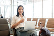 © bongkarn - An attractive Asian female passenger sits in the airport terminal with her laptop and belongings.