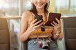 © bongkarn - A beautiful Asian female tourist is holding her smartphone and passport, waiting for her flight.