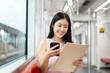 © bongkarn - A charming Asian female office worker is reading documents while taking a sky train to work.