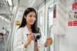 © bongkarn - A positive Asian female traveler is taking a picture with her camera in a sky train.