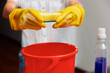 © SHOTPRIME STUDIO - Woman in yellow rubber gloves holding a sponge over a red bucket with a bottle of cleaning solution