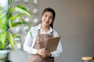 A friendly Asian female barista in an apron with a menu is standing in a minimalist coffee shop.