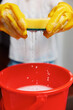 © SHOTPRIME STUDIO - Woman in yellow gloves holding a sponge over a red bucket with water flowing out