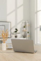 Wall Mural - A close-up image of a laptop computer on a wooden table in a minimalist white room.