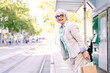 © Raul Mellado - smiling mature woman standing with shopping bags waiting for public transport, concept of sustainable mobility and urban lifestyle, copyspace for text