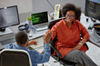 © Seventyfour - High-angle shot of smiling higher-weight female African American software engineer giving colleague high five celebrating success at large computer programmer desk in office