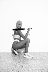 Wall Mural - Beautiful sexy woman in underwear. Model wearing bandit balaclava mask. Hot seductive female in nice lingerie posing near white wall in studio. Crime and violence. Monochrome