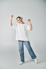 A stylish young woman in a white shirt and jeans strikes a pose against a neutral grey background.