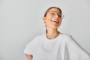 A young woman with glasses beams brightly in a crisp white shirt against a neutral grey backdrop.