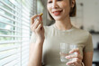 © itchaznong - Woman Taking Vitamin Pill with Water in Modern Home Setting, Emphasizing Healthy Lifestyle and Wellness