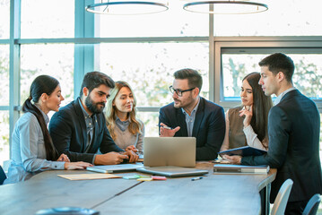 Business professionals using laptop for research and teamwork in a modern office, focusing on connection and collaboration.