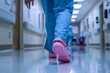 © Sourav Mittal - Close up of a nurse wearing blue scrubs and pink crocs walking in a hospital hallway, with a blurred background showing medical equipment, in a low angle shot from floor level, with the photo taken at