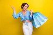 © deagreez - Portrait of overjoyed nice girl with short hair wear blue blouse hold shopping bags raising palm up isolated on yellow color background