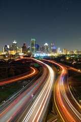 Wall Mural - Highway Overlook at Night. An overlook above a busy highway, with streams of car lights creating long, glowing trails. The city's skyline is illuminated in the background