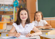 © malyutinaanna - A cute girl sits in a classroom at a table with notebooks and textbooks. The student writes in a notebook. Back to school. School supplies. Student at a lesson, class during a lesson.