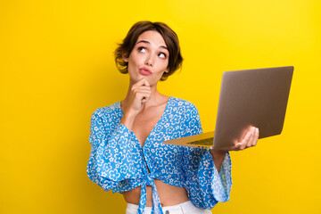 Poster - Portrait of puzzled girl with short hair wear blue blouse hold laptop thoughtfully look empty space isolated on yellow color background