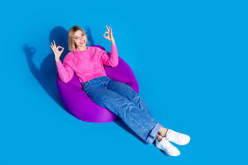 Canvas Print - Full body portrait of nice young woman beanbag okey symbol wear sweater isolated on blue color background