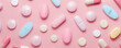 © Volodymyr - An overhead view of different shaped and colored pills arranged neatly on a pastel pink background. The soft color palette provides a calm and clean space for text in the center of the image.