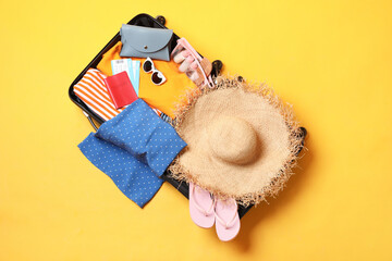 Wall Mural - Open suitcase with traveler's belongings on yellow background, top view