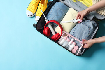 Canvas Print - Woman packing suitcase on light blue background, top view. Space for text