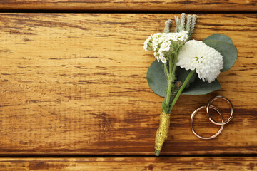 Wall Mural - Small stylish boutonniere and rings on wooden table, flat lay. Space for text