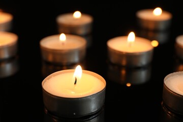 Wall Mural - Many burning tealight candles on black background, closeup