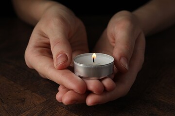 Sticker - Woman holding burning tealight candle at wooden table, closeup