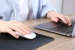 © New Africa - Woman using computer mouse while working with laptop at wooden table, closeup