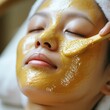 © suratin - Golden Glow: Woman enjoying a luxurious gold facial mask application, embracing skincare and self-care for radiant skin.