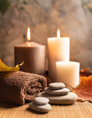 Wall Mural - Cozy spa setting with candles, smooth stones, soft towels and autumn leaves on warm wooden surface. Relaxation and meditation. Wellness, body and healthcare.