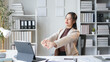 © amnaj - Young businesswoman takes a break at her office desk, stretching to relieve stress and promote workplace wellness