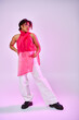 © LIGHTFIELD STUDIOS - An African American woman poses confidently in a pink shirt and white pants against a vibrant backdrop.