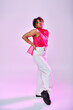 © LIGHTFIELD STUDIOS - African American woman posing actively in pink top and white pants on vibrant backdrop.