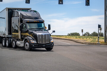 Wall Mural - Shiny black big rig semi truck transporting cargo in dry van semi trailer turning on the crossroad intersection with traffic light