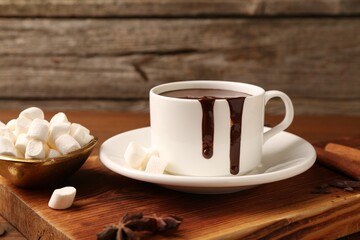 Wall Mural - Tasty melted chocolate in cup and marshmallows on wooden table, closeup