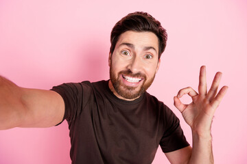 Poster - Photo of satisfied impressed guy with stylish stubble dressed brown t-shirt making selfie showing okey isolated on pink color background